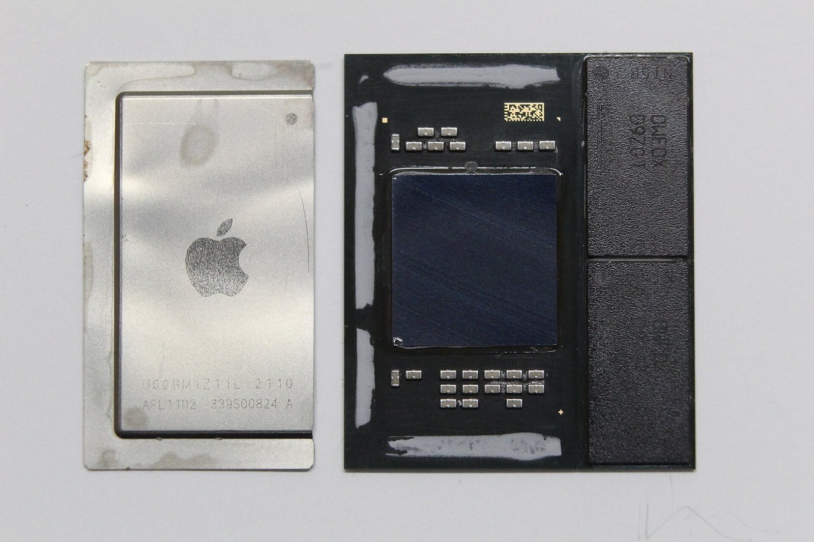 An Apple M1 package with its metal lid lifted off and laid beside it: a dark square die in the middle and two black rectangular chips on the right