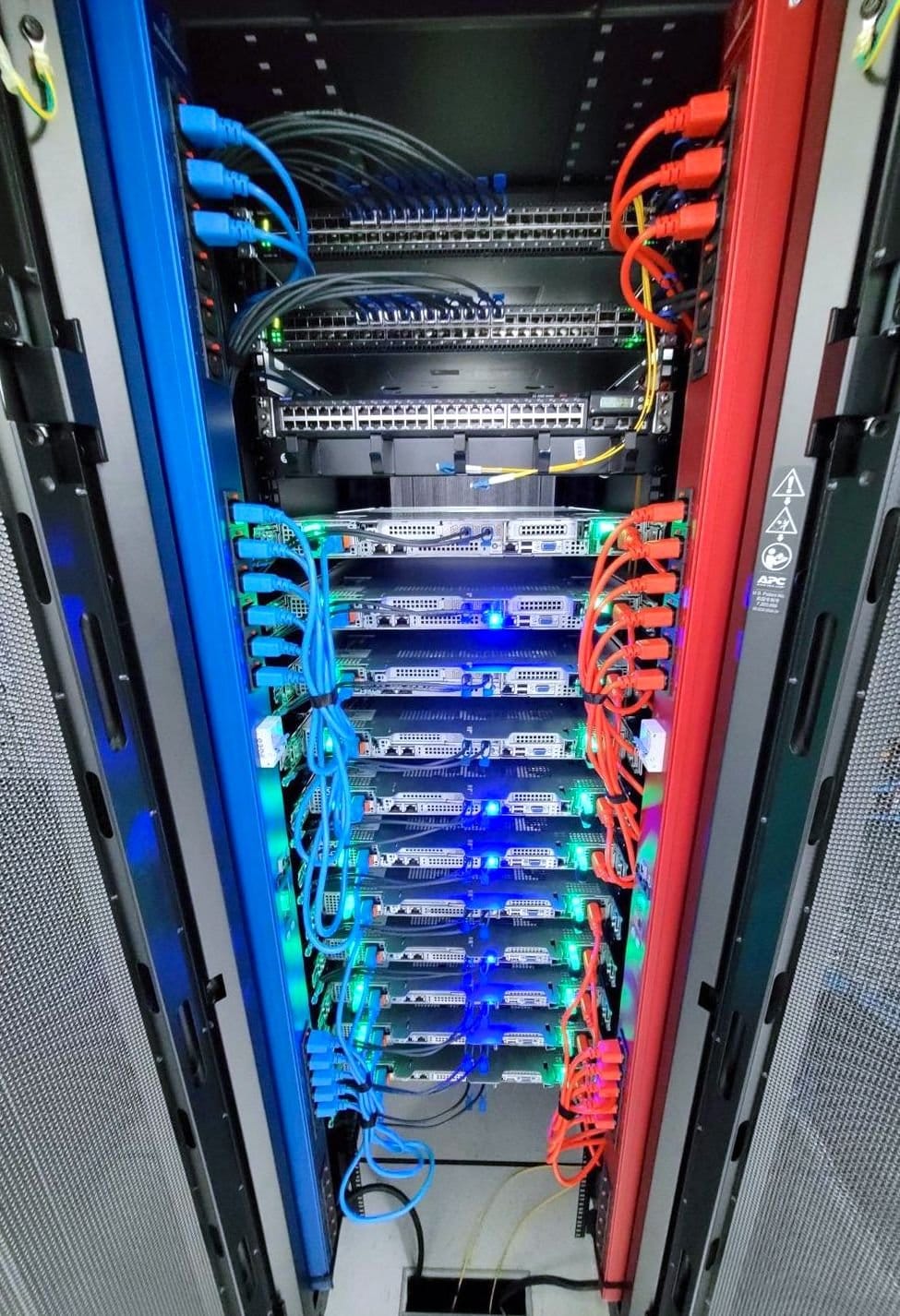 An open server rack with a blue power strip running down the left side and a red one down the right, each server plugged into both