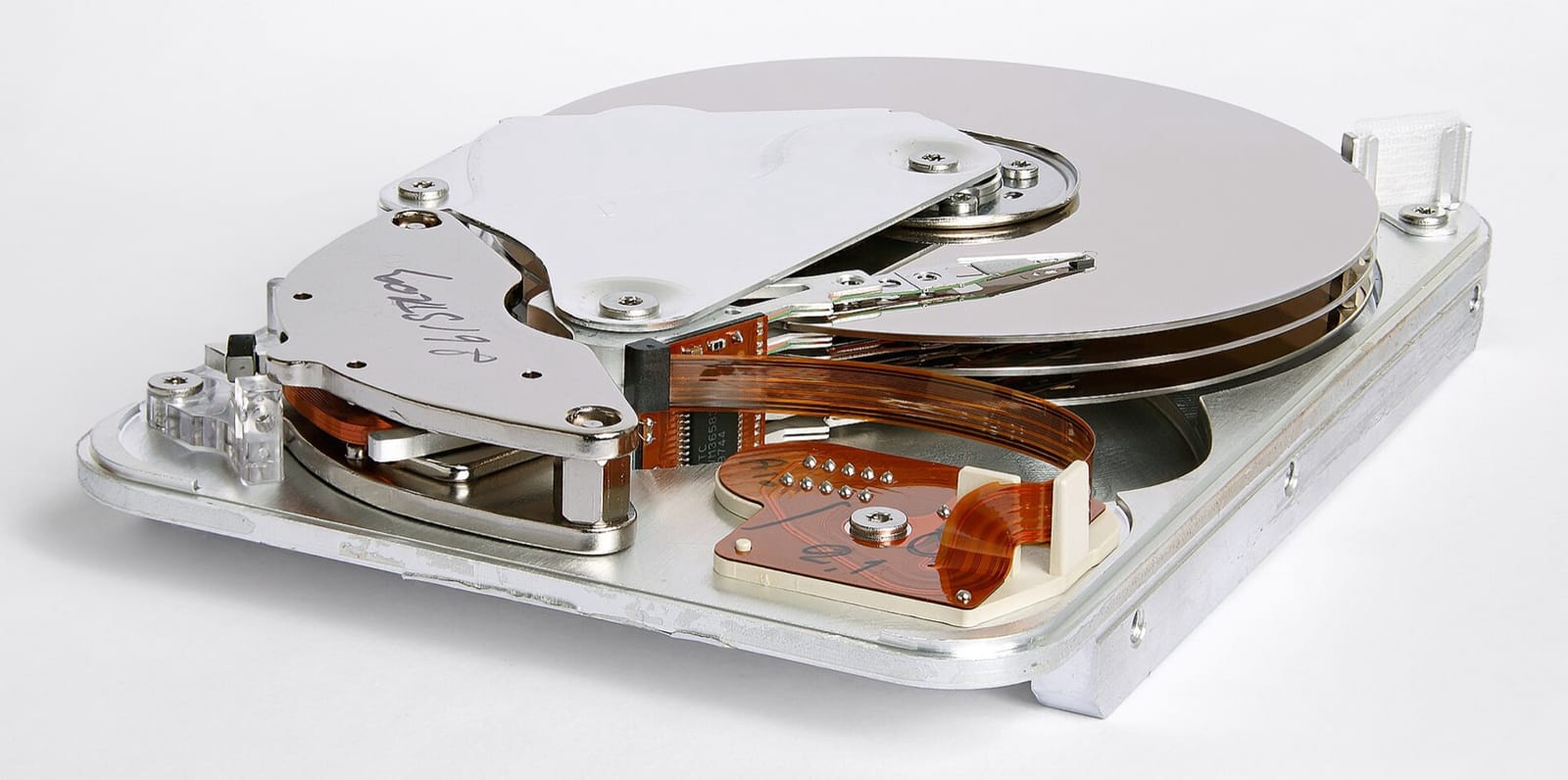 An opened 3.5-inch hard drive showing two stacked silver platters, the actuator arm holding the read/write heads, and a ribbon cable