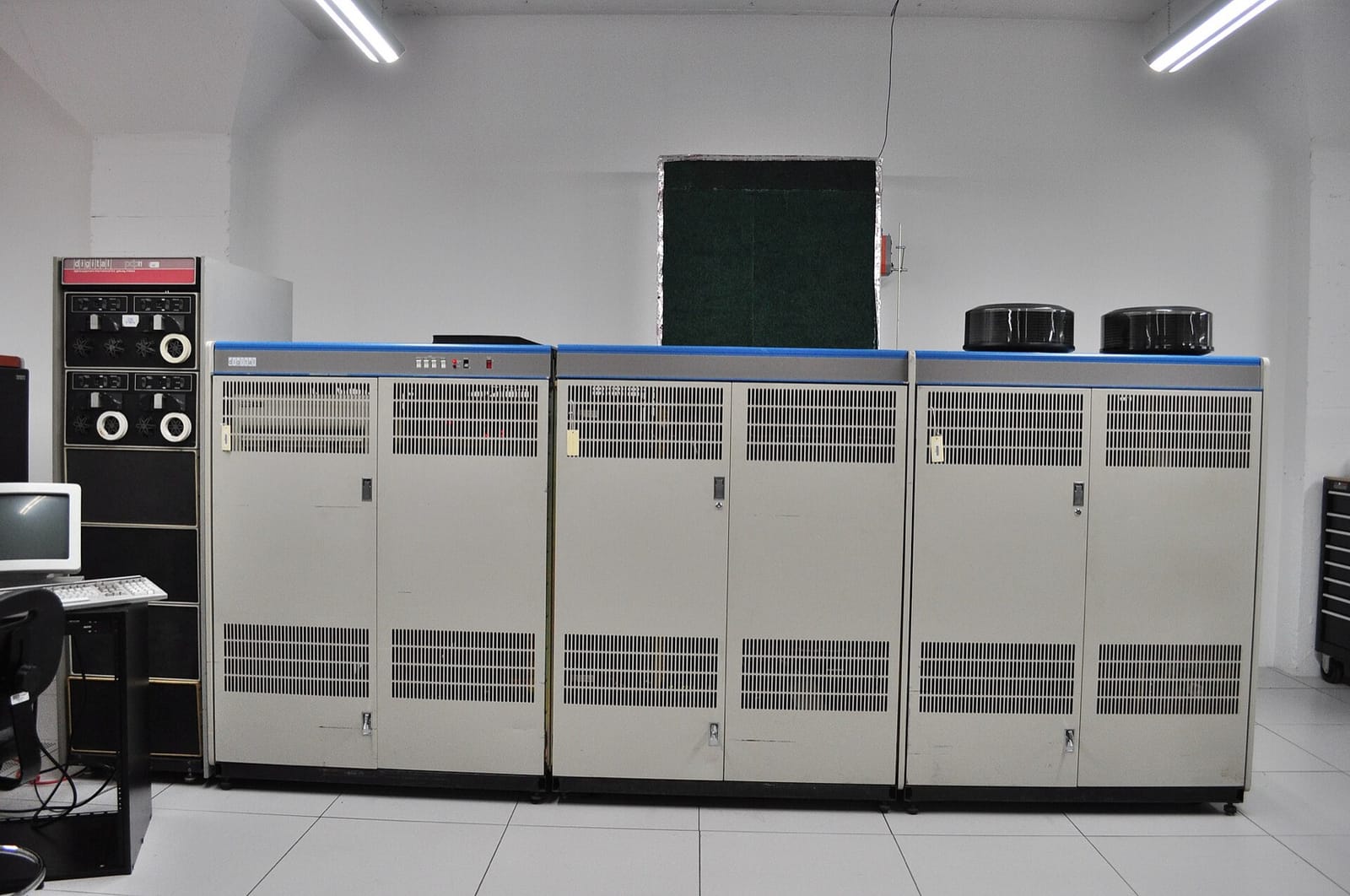 A row of tall cream-coloured cabinets with blue tops making up a DECsystem-10 computer, with tape drives at the left and a terminal on a desk
