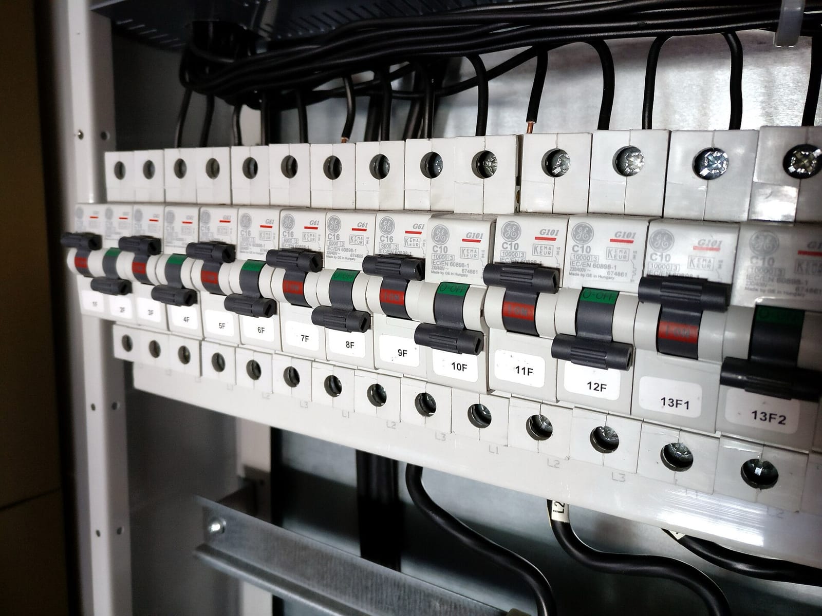 A row of miniature circuit breakers clipped onto a rail inside an open electrical cabinet, each with a toggle and a numbered label