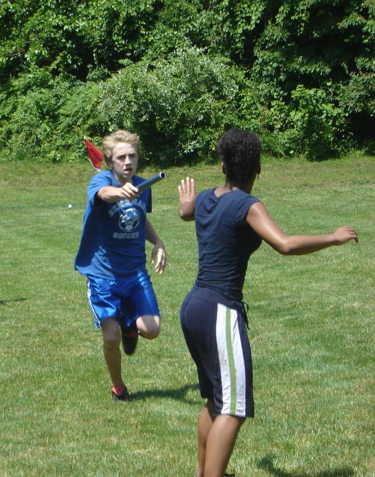 A runner holding out a relay baton to a teammate who is reaching back for it