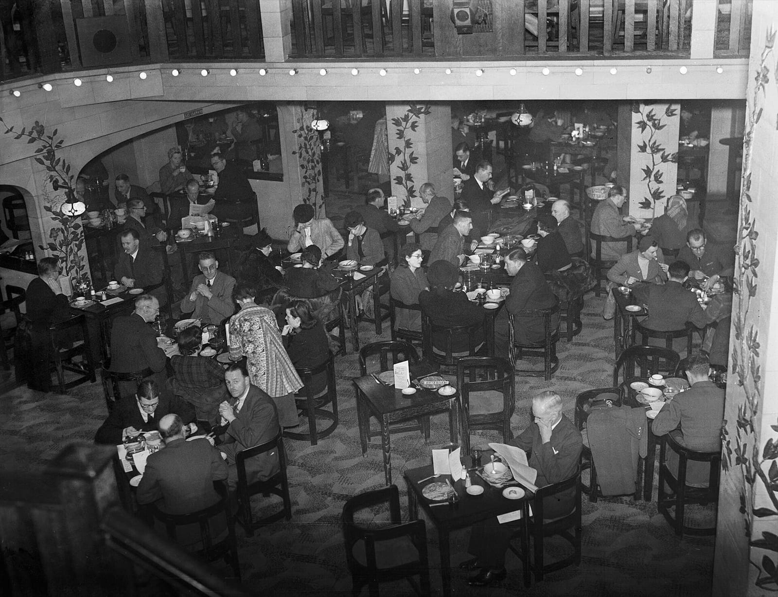 A black-and-white photograph looking down on a crowded restaurant, with diners at small tables