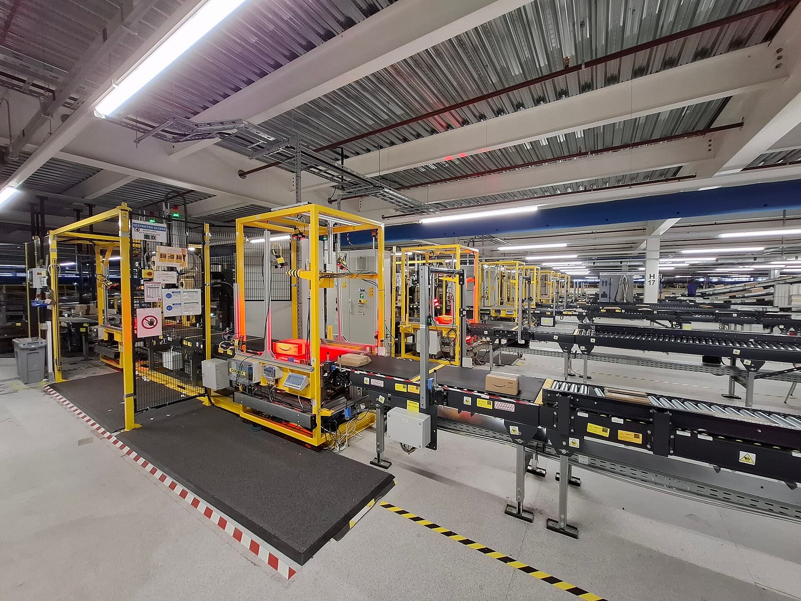 Yellow-framed machines over a conveyor, scanning and labelling cardboard boxes, with long conveyor lines behind