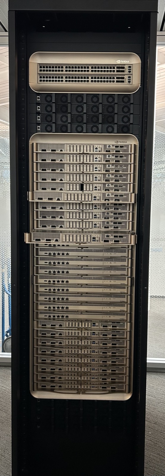 A tall liquid-cooled server rack with stacked gold-fronted compute trays and NVLink switch trays