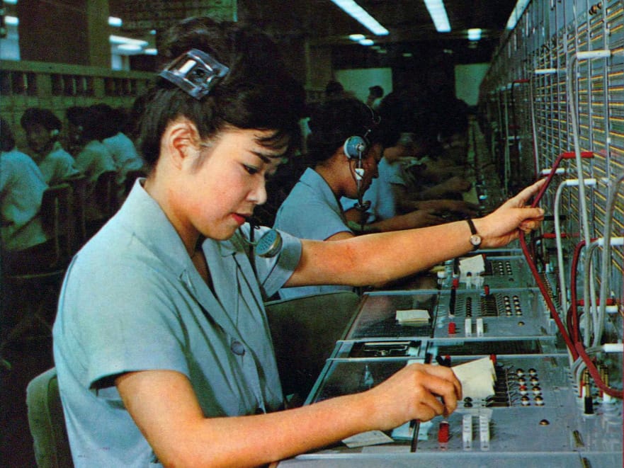 Telephone operators wearing headsets connecting calls with cords at a long switchboard