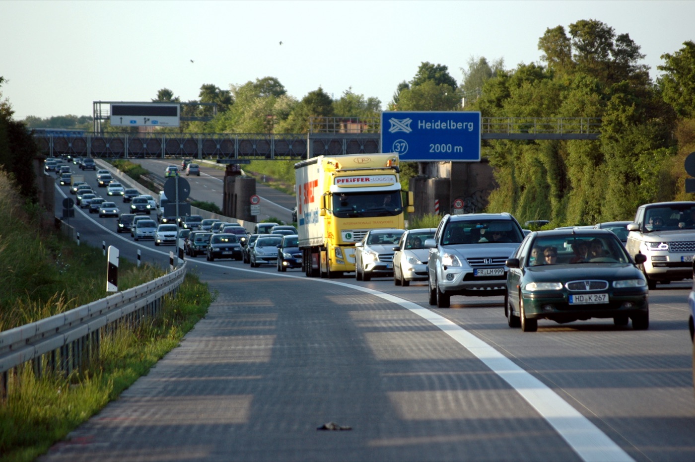 A queue of cars and lorries on a German motorway near a sign for Heidelberg, with the queue stretching back into the distance