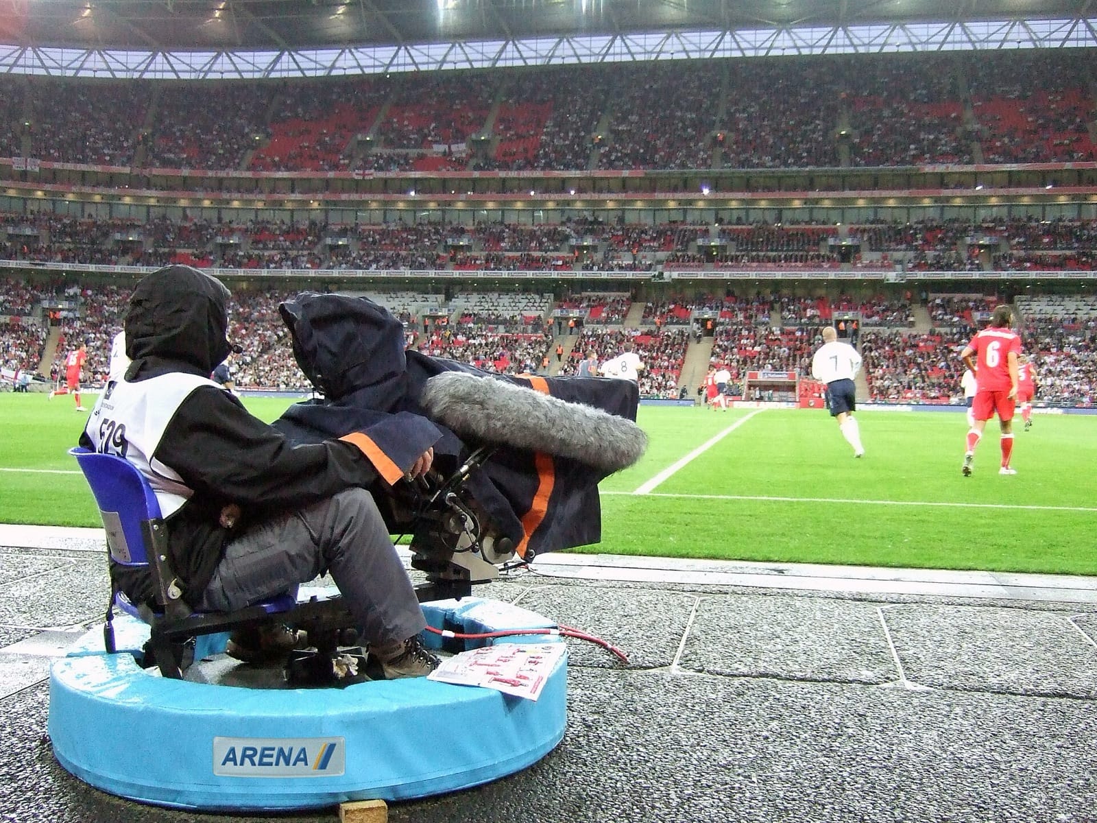 A broadcast television camera with a long zoom lens at a football stadium
