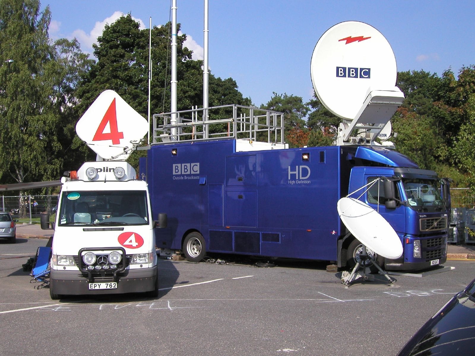 Two satellite uplink trucks with dish antennas parked at a sports event