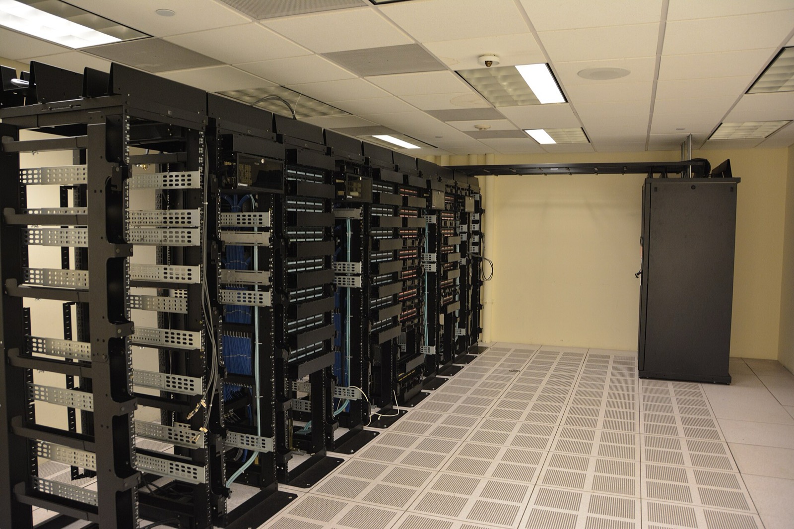 A row of open server racks with blue and white network cabling over a raised perforated floor