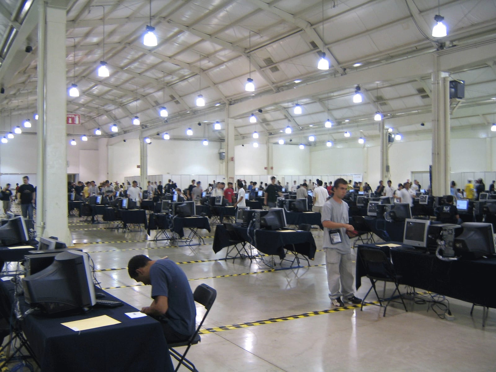 A large hall full of rows of tables with computer monitors, with contestants working at them