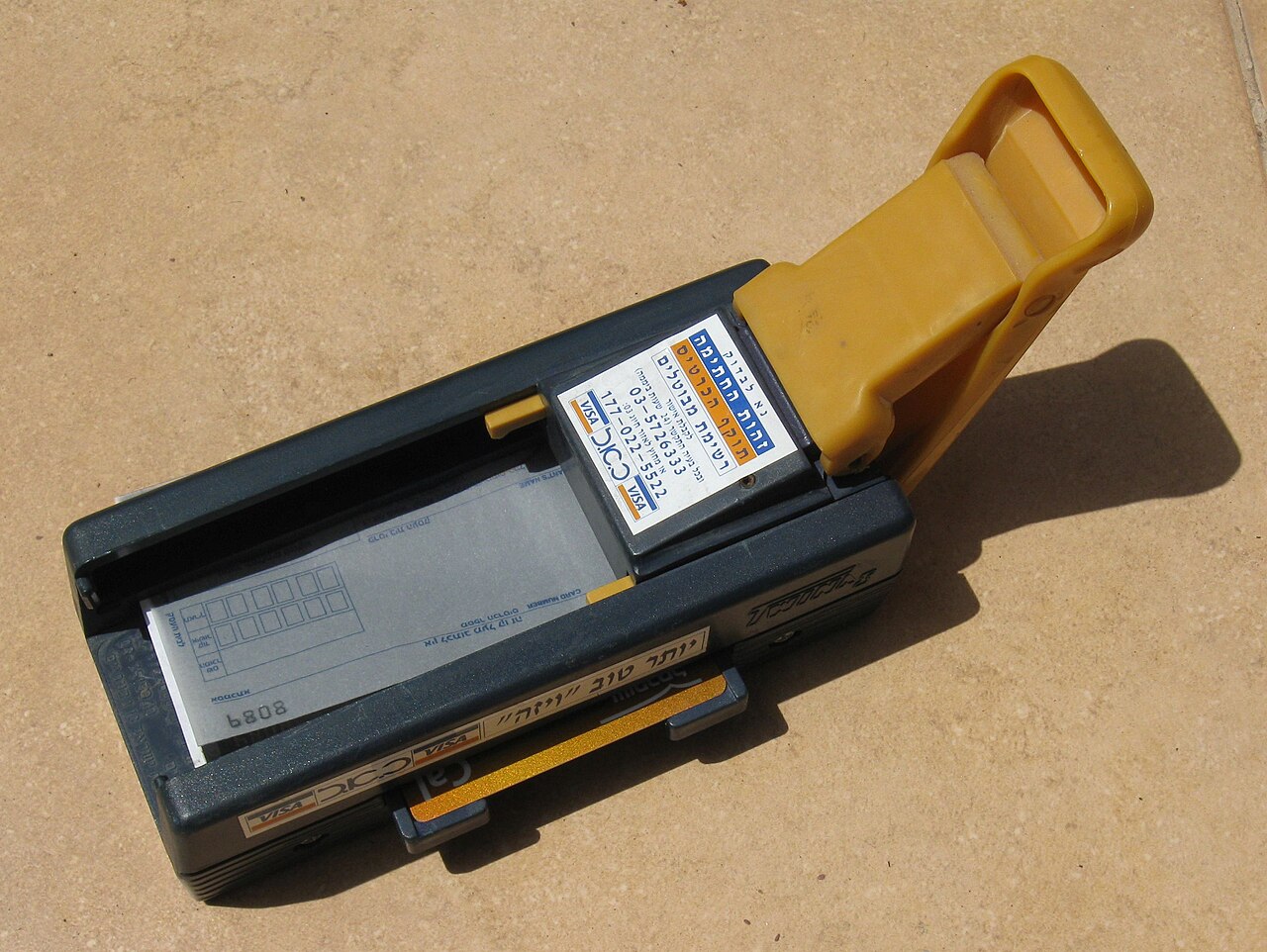 A manual credit card imprinter with a card in its bed and a blank carbon slip inserted, seen from above