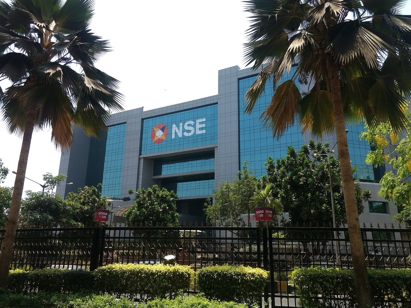 The NSE building in Mumbai, a glass-fronted office block with a large NSE logo, seen through palm trees