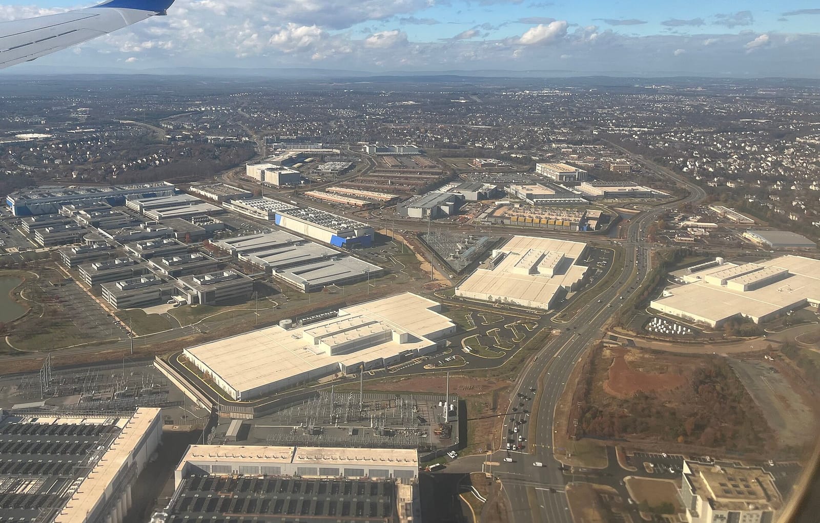 Aerial view of many large flat-roofed data centre buildings and electrical substations among roads and housing near Ashburn, Virginia